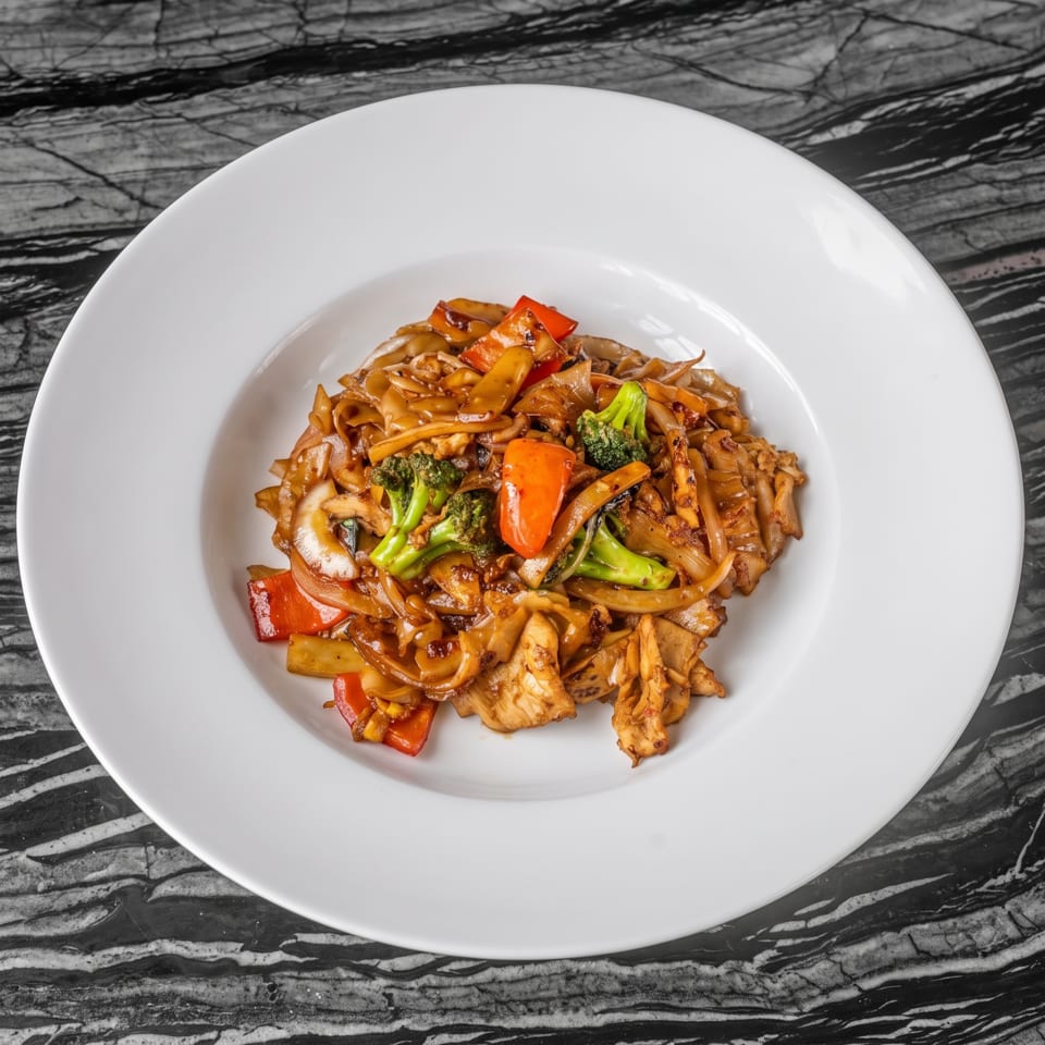 Stir-fried noodles with chicken, broccoli, red peppers, and onions on a white plate.