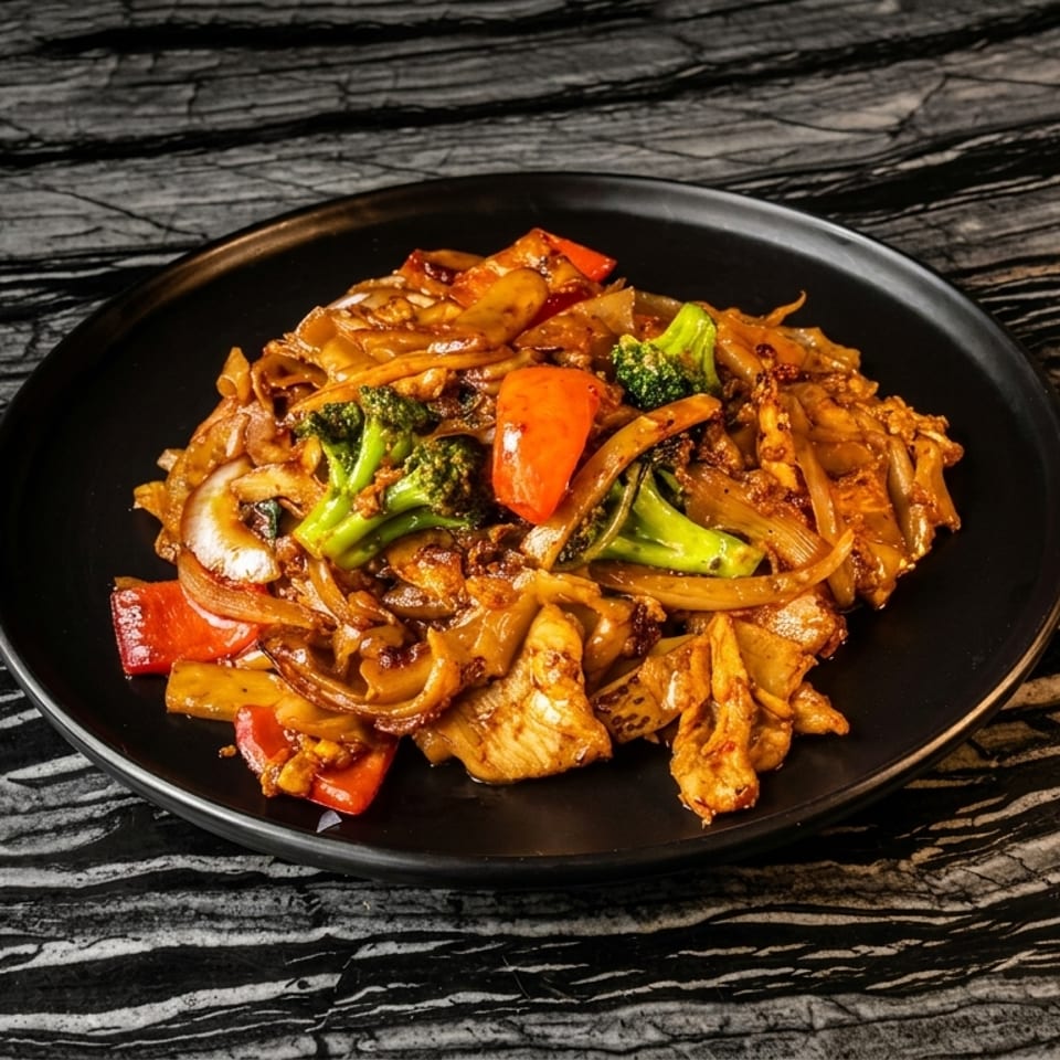 Stir-fried noodles with chicken, broccoli, red peppers, and onions on a black plate.