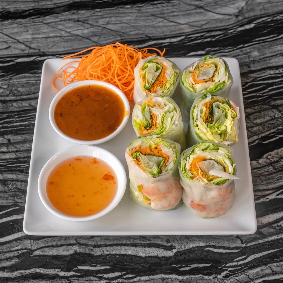 Six fresh spring rolls with shrimp, lettuce, and carrots, served with two dipping sauces and shredded carrots.